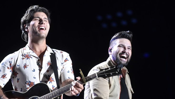 two men singing and playing guitars on stage