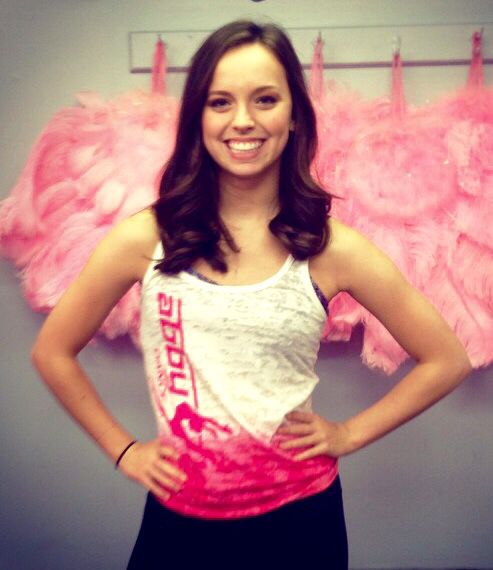 a woman standing in front of a wall with pink feathers hanging on it's sides