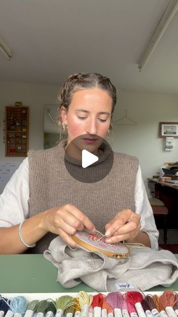 a woman sitting at a table working on a piece of fabric