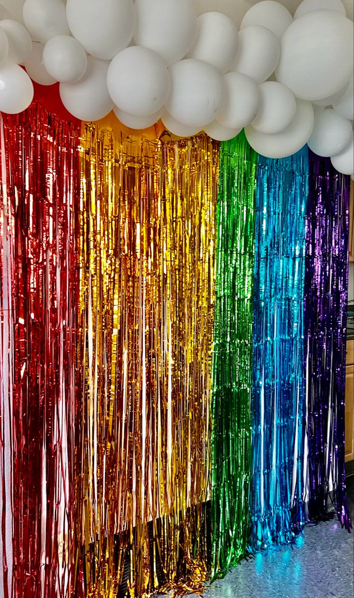 balloons and streamers are hanging in front of a rainbow colored backdrop at a party