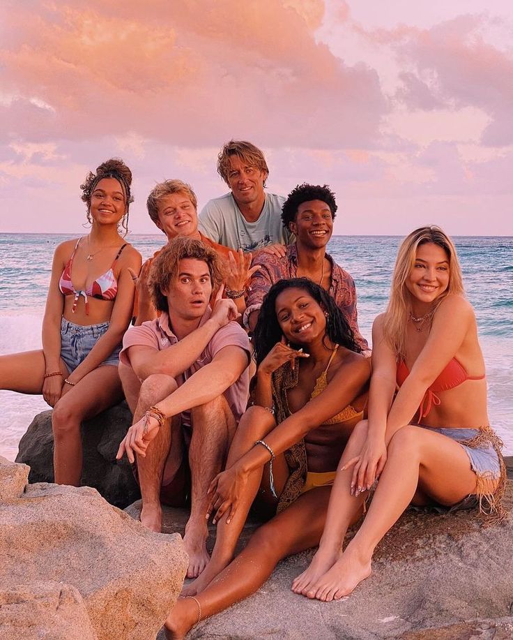 a group of young people sitting on top of rocks near the ocean at sunset or dawn