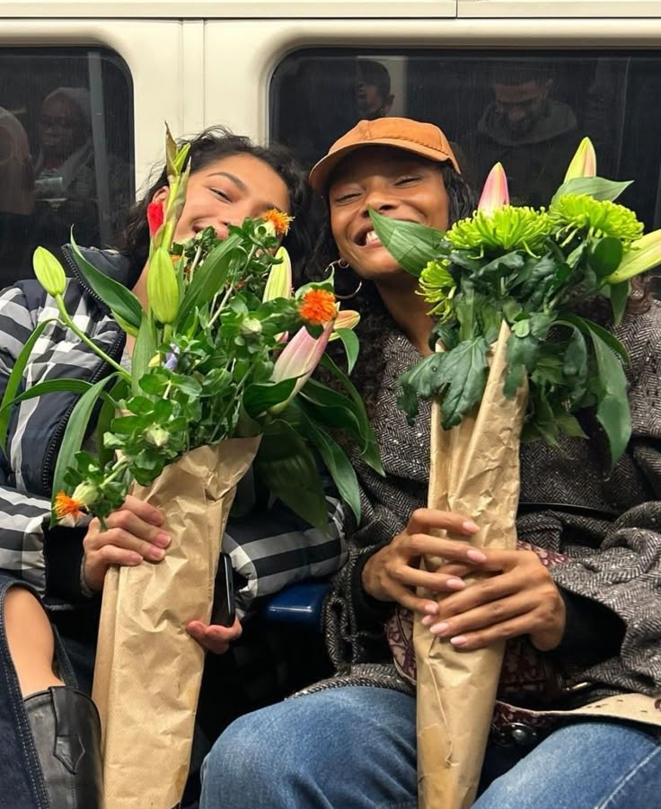 two people sitting on a train with flowers in their hands and one person holding a paper bag