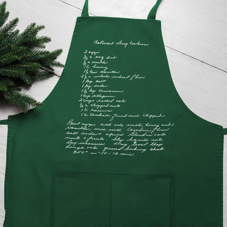 a green apron with writing on it next to a potted plant and pine needles