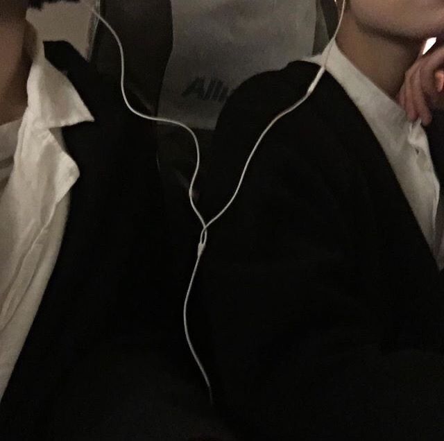 two young men sitting next to each other with headphones in their ears and one holding a cell phone