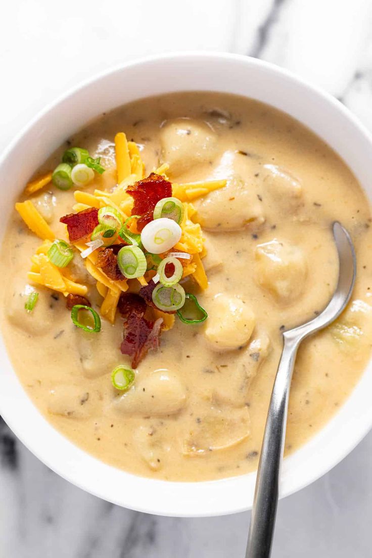 a white bowl filled with soup on top of a marble counter next to a spoon