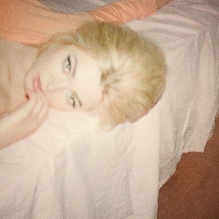 a woman laying in bed with her head on the pillow and looking at the camera