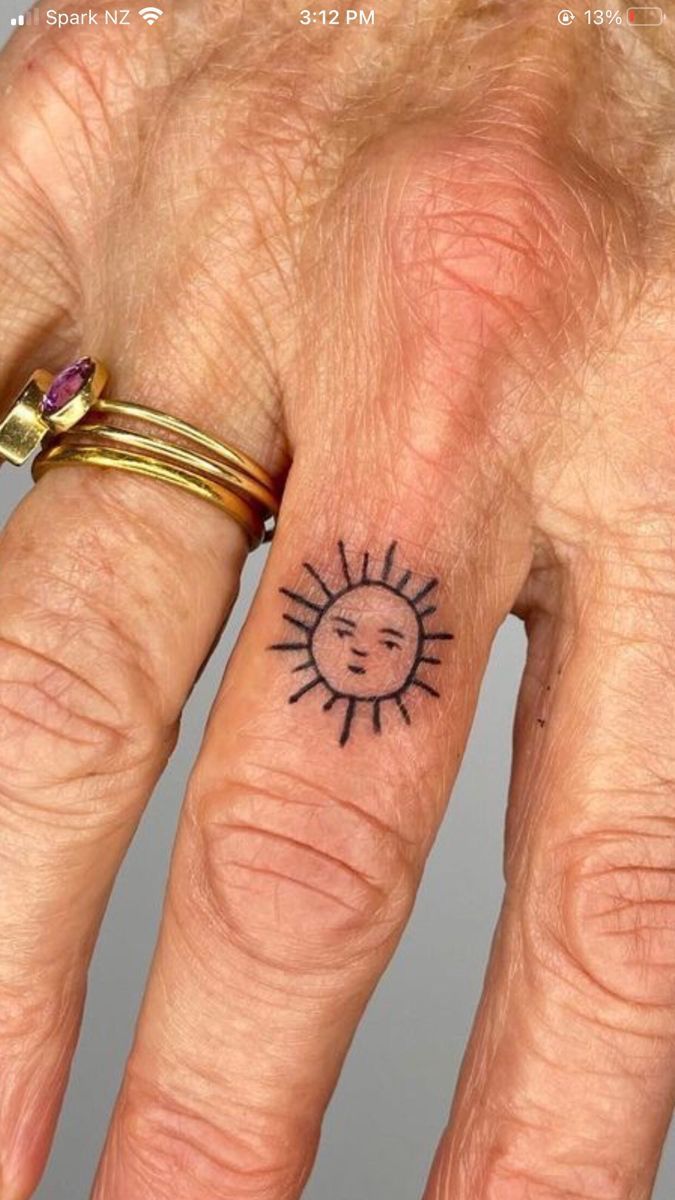 a woman's hand with a small sun tattoo on her left ring finger,