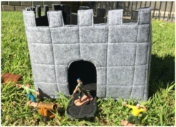 there is a castle made out of felt and plastic toys on the grass in front of it