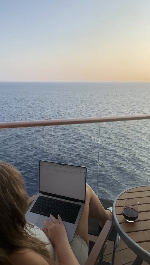 a woman sitting at a table on top of a boat working on her laptop computer