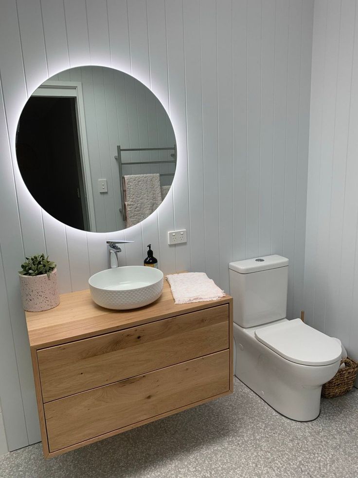 a white toilet sitting next to a wooden dresser under a round mirror in a bathroom