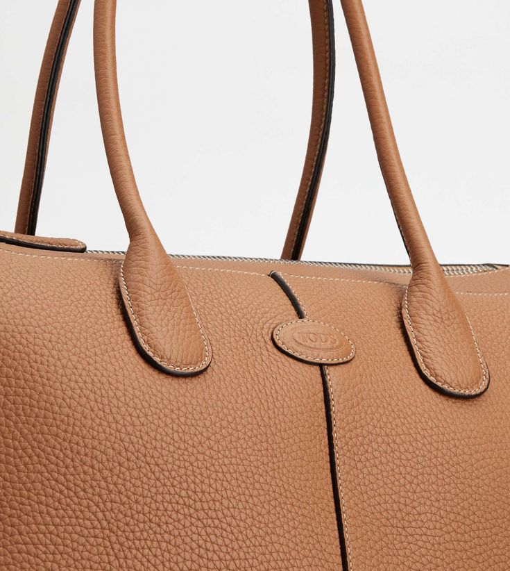 Central ribbing and tubular handles characterize this elegant shopping bag with Tod's logo stamped on the front. Featuring an internal pouch, it is crafted in soft calfskin leather. To accompany with class and femininity your everyday outfits. Brown Calf Leather Bag With Handles, Designer Double Handle Bag With Rolled Handles, Brown Business Bags With Round Handle, Tan Calf Leather Travel Bag, Cognac Calf Leather Bag With Handles, Cognac Leather Bag With Round Handle, Classic Cognac Shopping Bag, Cognac Calf Leather Bag With Top Carry Handle, Luxury Tan Business Bags