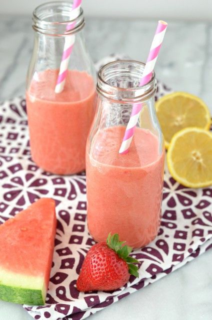 two mason jars filled with watermelon smoothie next to sliced lemons and strawberries