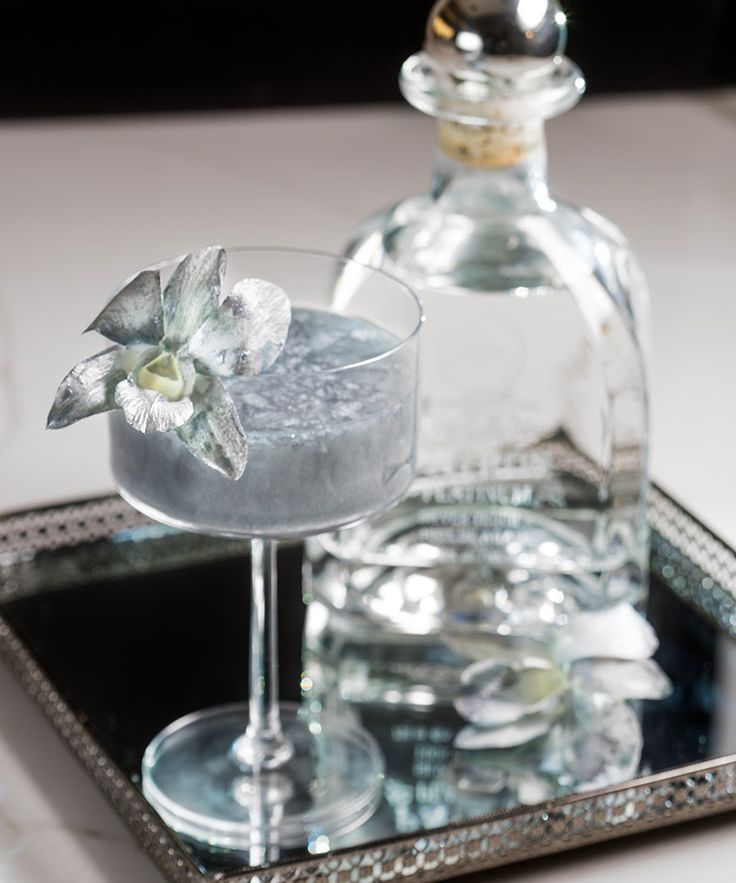 a glass filled with liquid sitting on top of a metal tray next to a bottle