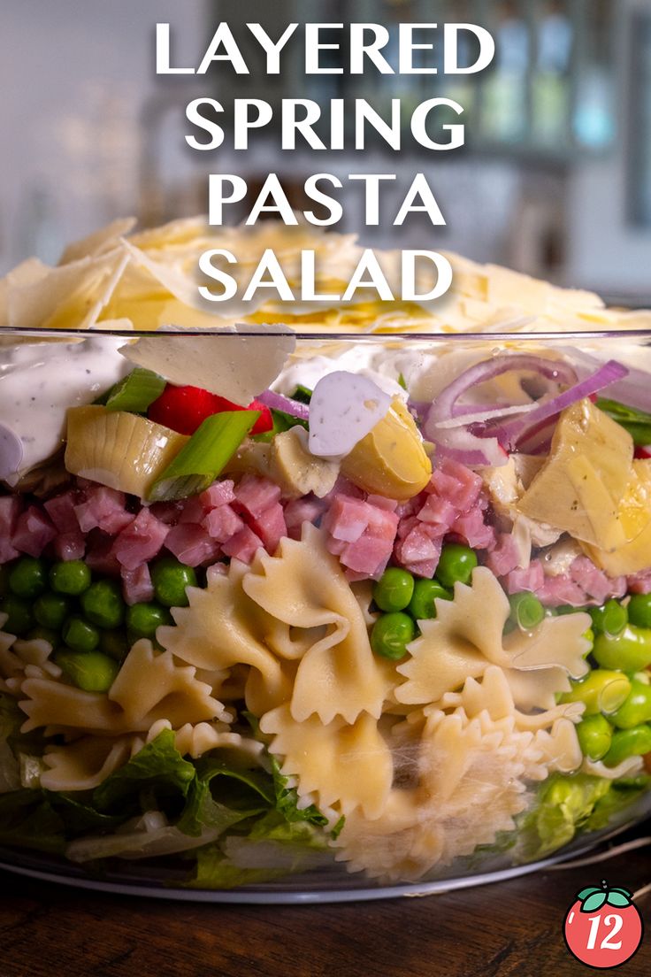 layered spring pasta salad in a glass bowl with text overlay that reads layered spring pasta salad