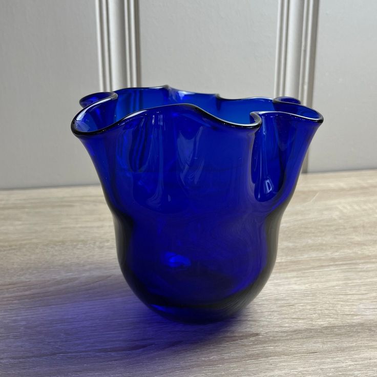 a blue glass vase sitting on top of a wooden table next to a white wall