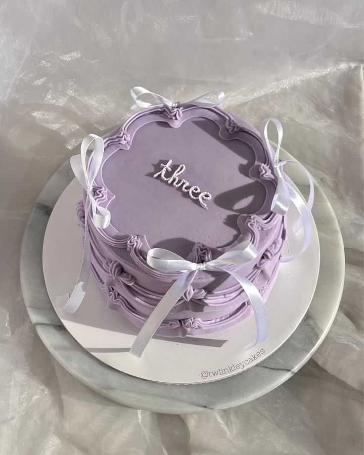 a purple cake with white ribbons and the word peace on it sitting on a plate