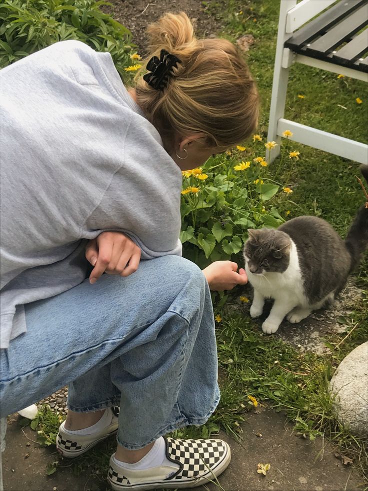 a woman kneeling down petting a cat on the ground