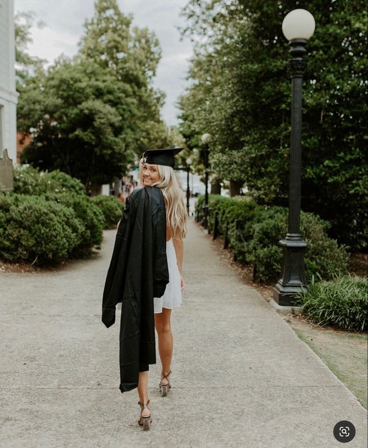 a woman is walking down the sidewalk in her graduation gown