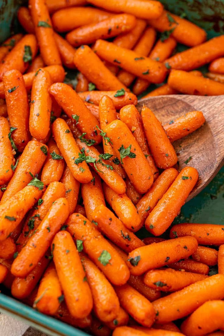 a wooden spoon full of cooked carrots in a green dish with parsley on top