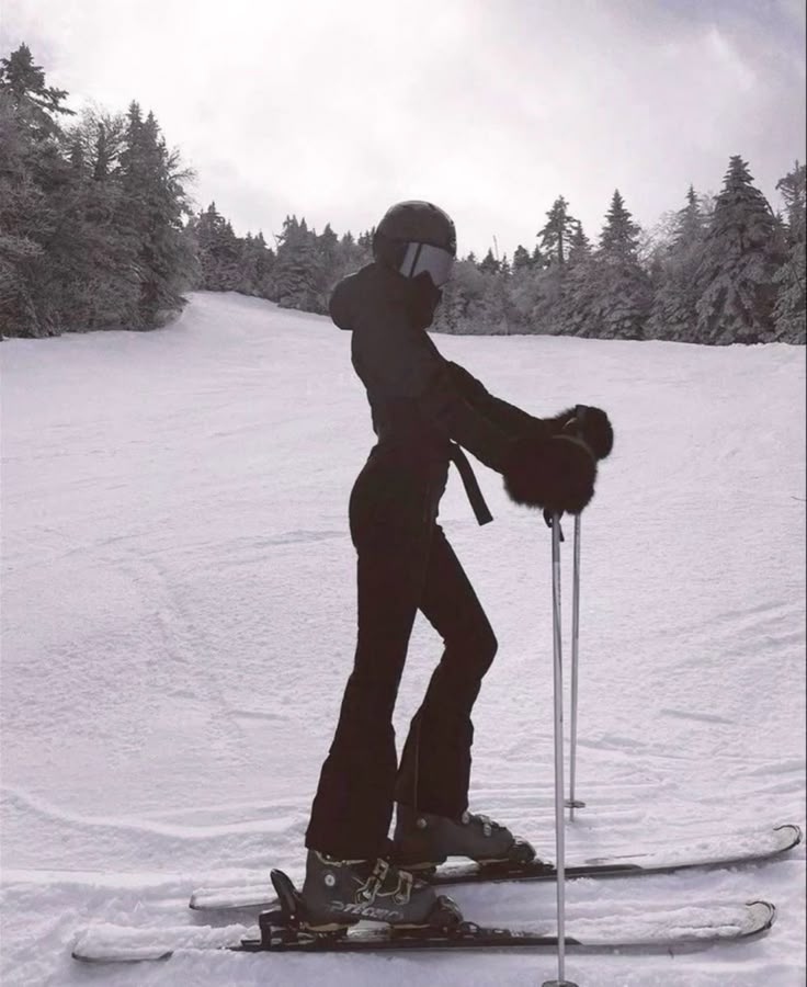 a person riding skis on top of a snow covered slope with trees in the background