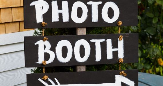 a wooden sign that says photo booth with an arrow on it and flowers in front