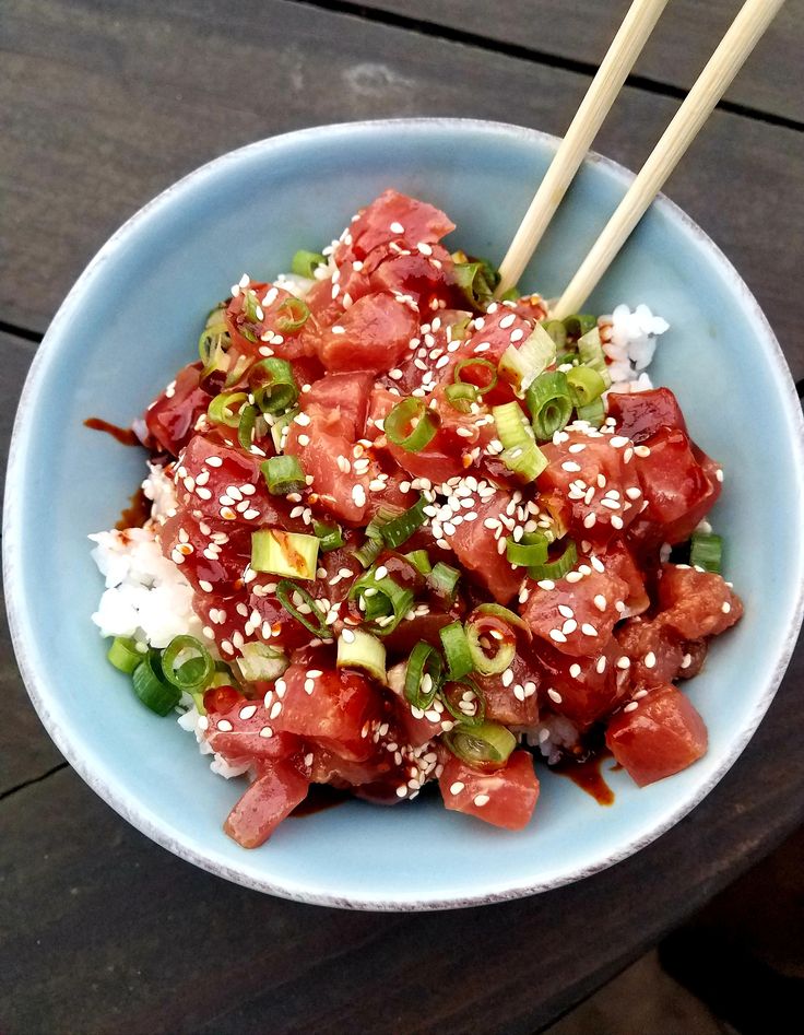 a blue bowl filled with food and chopsticks on top of a wooden table