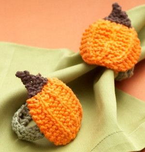 two knitted pumpkins are sitting on top of a green napkin, one is orange and the other is gray