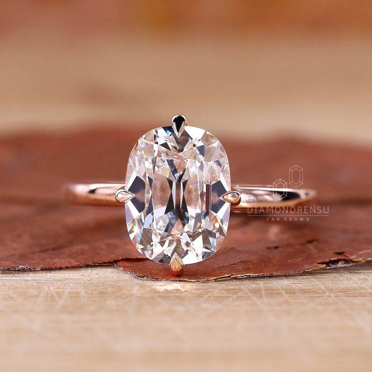 an oval cut diamond ring sitting on top of a leaf