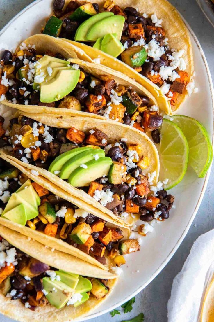 three tacos with black beans, corn and avocado on a white plate