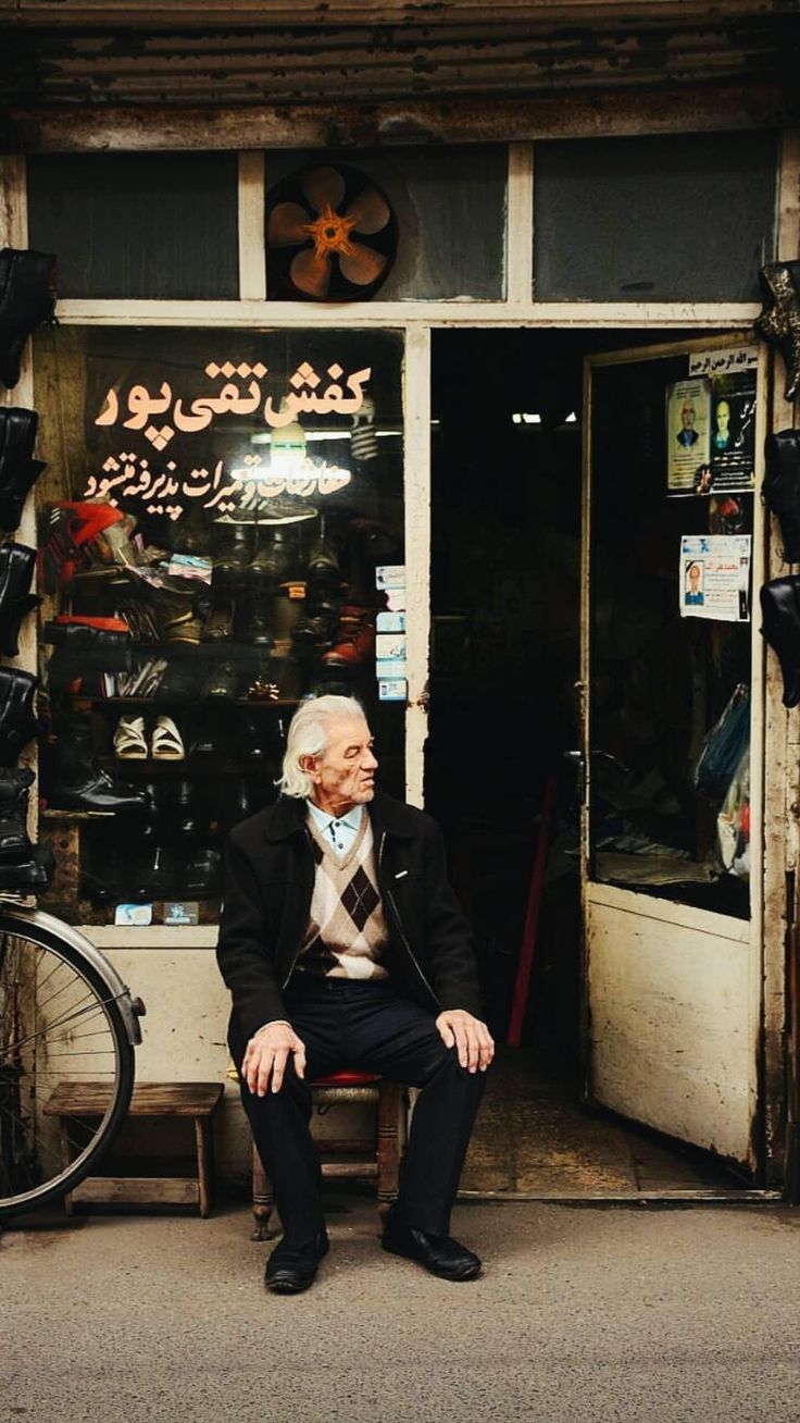 an old man sitting on a bench in front of a shop