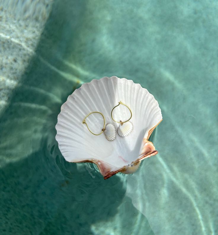 Dive into the elegance of the ocean with our Marina Shell Hoop Earrings. These stunning hoops, featuring natural shell accents, bring a touch of seaside charm to any outfit.  Each pair of Marina Shell Hoop Earrings is adorned with authentic, ethically-sourced shells from the coast of Englewood Beach. Summer Beach Hoop Earrings, White Beaded Hoop Earrings For Beach, Handmade Hoop Earrings For The Beach, White Shell-shaped Hoop Earrings, White Small Hoop Jewelry For The Beach, White Small Hoop Earrings For Beach, Small Hoop Earrings For Summer Beach, White Hoop Earrings For Vacation, Small Hoop Earrings For Vacation