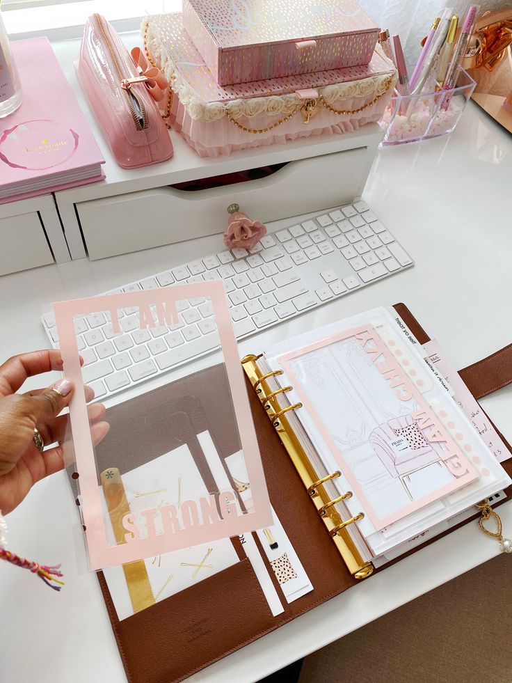 a person is holding a pink binder in front of a desk with various items on it