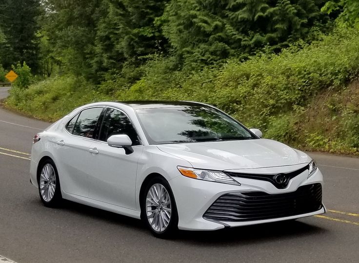 a white toyota camry driving down a road next to green trees and bushes on either side of the road