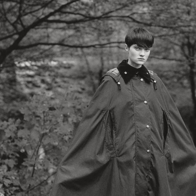 a young man is standing in the woods wearing a raincoat