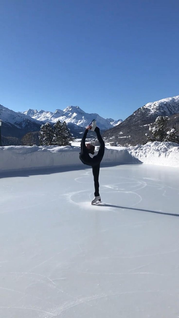 a person doing a hand stand on an ice skating rink with mountains in the background