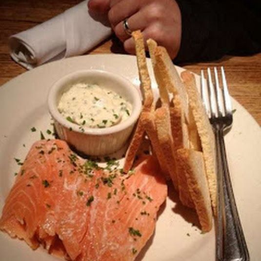 a white plate topped with fish and bread next to a bowl of dip on top of it