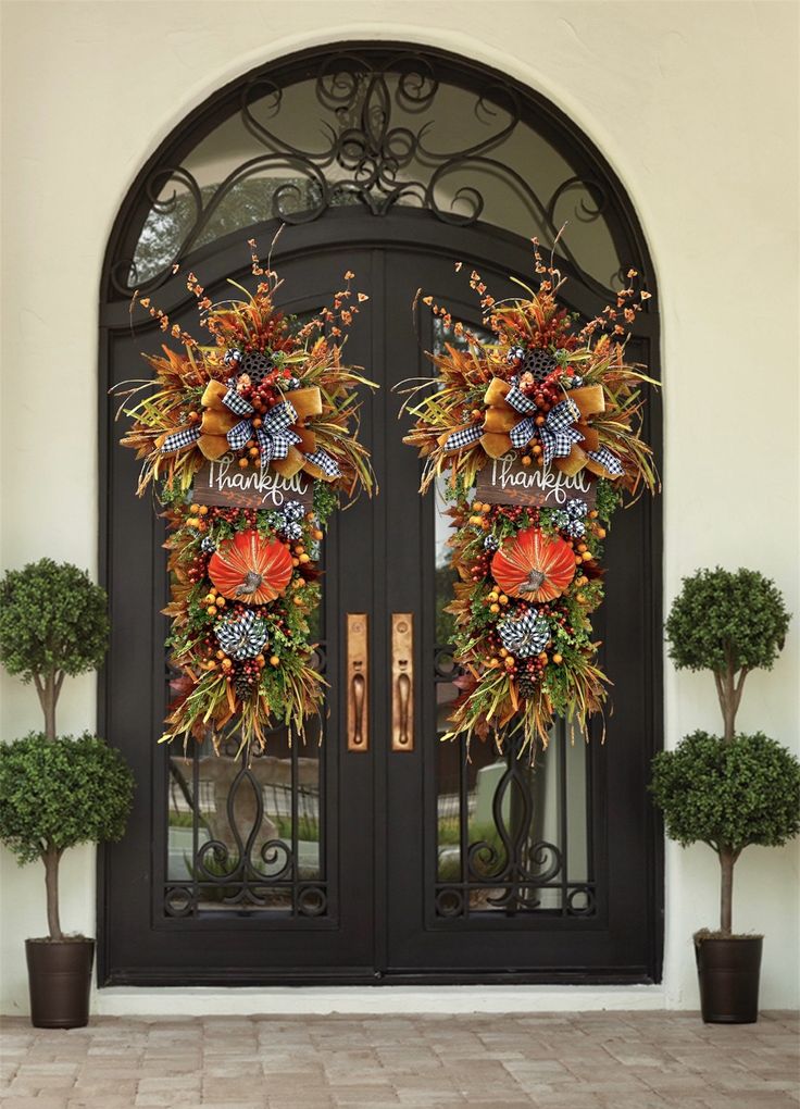 two wreaths on the front door of a house with thanksgiving decorations hanging from them