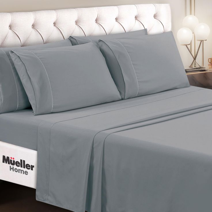 a bed with grey sheets and pillows on it