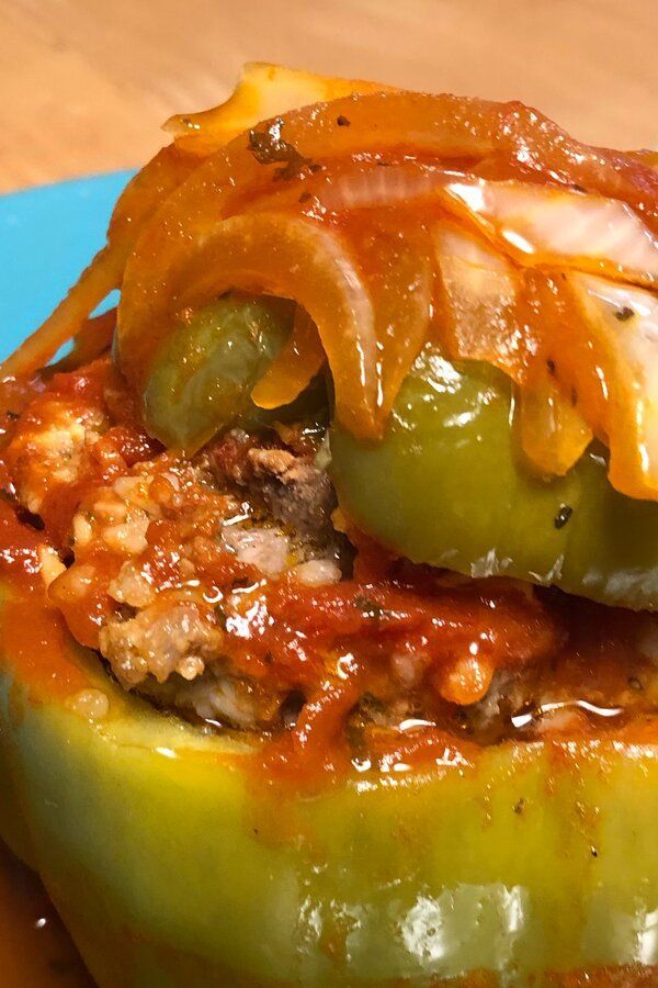 a green pepper stuffed with meat and cheese on a blue plate next to a wooden table