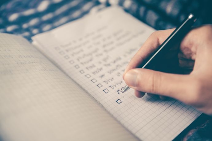 a person holding a pen and writing on a notebook with a check book in front of them