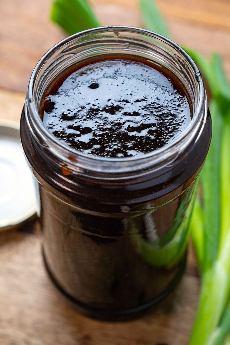 a jar filled with black liquid sitting on top of a wooden table next to green leaves