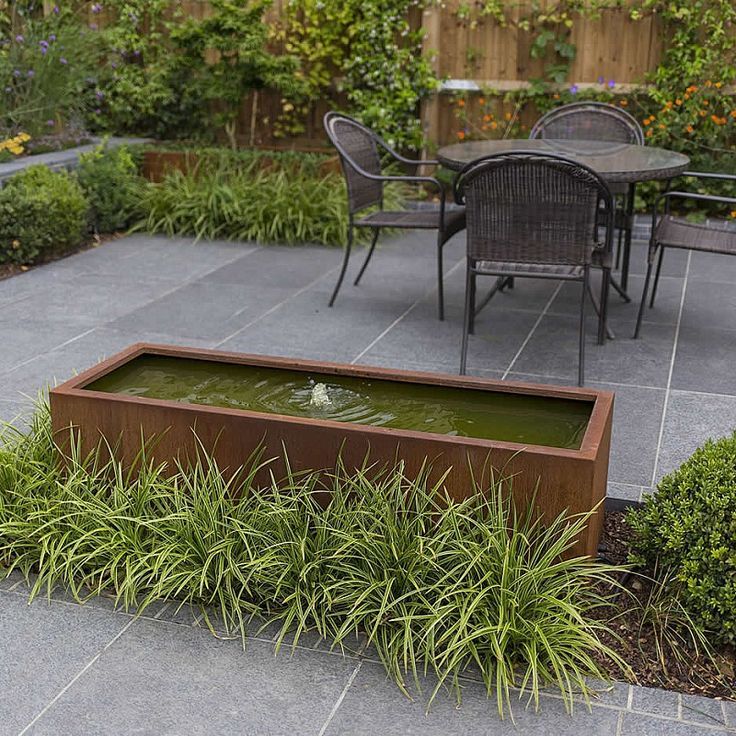 an outdoor patio with a water feature and dining table in the back ground, surrounded by greenery