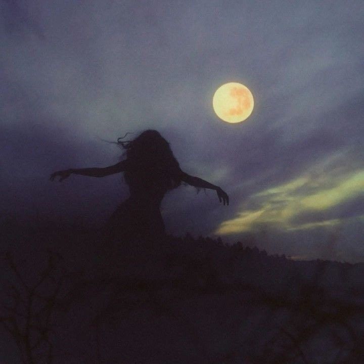 the silhouette of a woman with her arms outstretched in front of a full moon at night