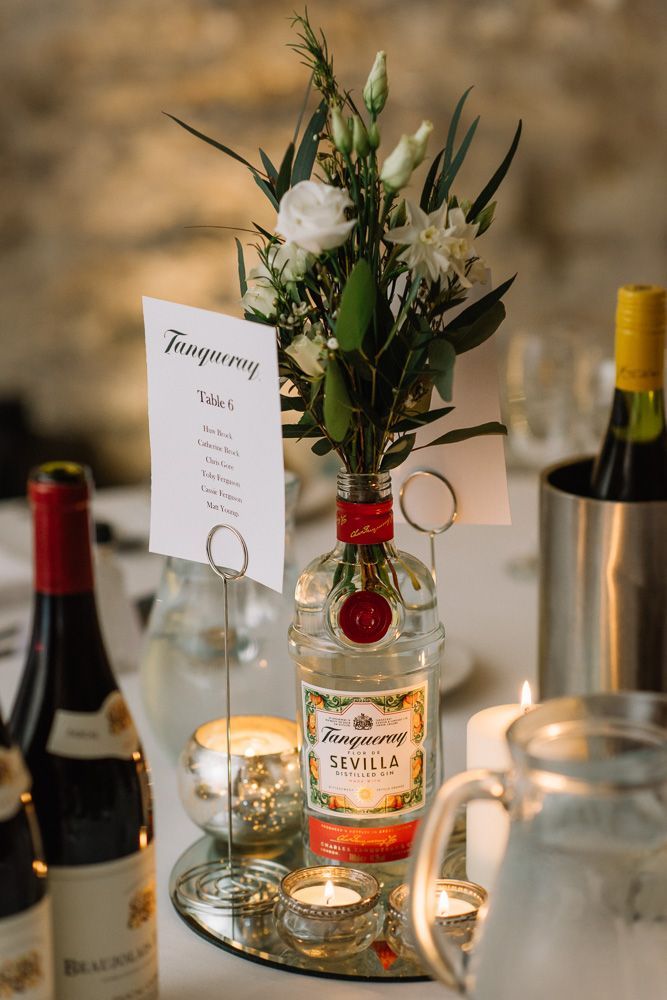 a table topped with bottles of wine and flowers on top of a glass plate next to candles