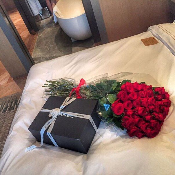 a bouquet of red roses and a gift wrapped in black paper on top of a bed