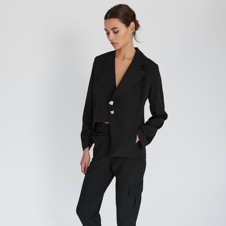 Asymmetry is everything for this black blazer jacket. Asymmetric hem, only one lapel (collar), triangle shape on one side and two different sized buttons,  Defined by its asymmetric details, this comfy chic blazer is tailored to stand out!  It has padded shoulders and boxy shape for structure.  Complete the look with Arya Tapered Pants to suit up! %20 Lyocell %80 Polyester  Dry Clean Only Chic Asymmetrical Spring Blazer, Chic Asymmetrical Blazer For Spring, Asymmetrical Spring Blazer For Formal Events, Asymmetrical Spring Formal Blazer, Asymmetrical Blazer For Spring Formal, Asymmetrical Blazer For Spring Formal Events, Chic Asymmetrical Semi-formal Blazer, Elegant Asymmetrical Single-breasted Outerwear, Semi-formal Asymmetrical Chic Blazer