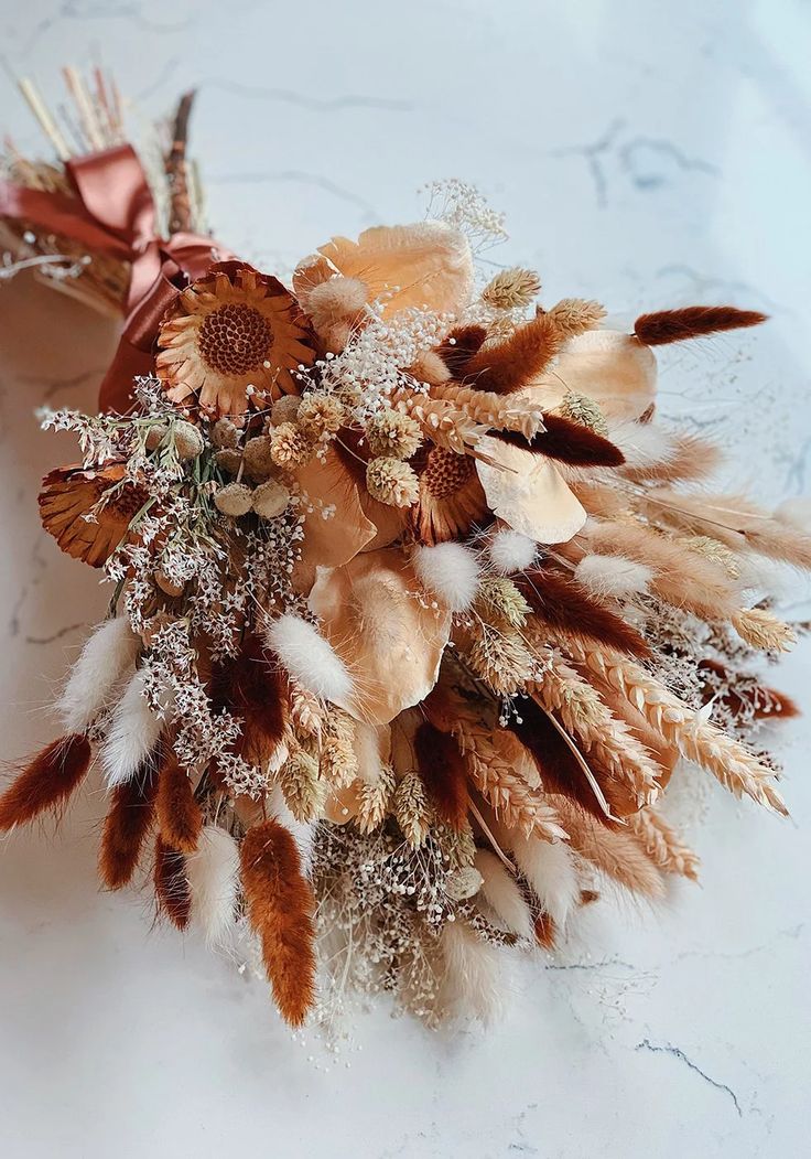 an arrangement of dried flowers and feathers on a table