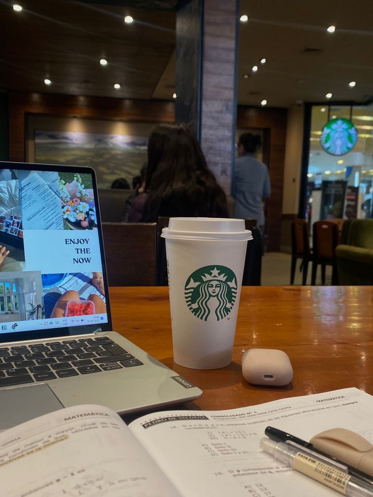 a starbucks cup sitting on top of a wooden table next to an open laptop computer