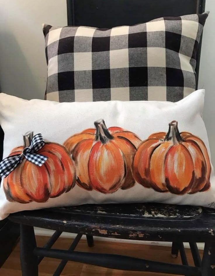 a pillow with three pumpkins on it sitting on a chair next to a plaid pillow