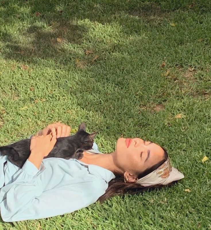 a woman laying in the grass holding a cat